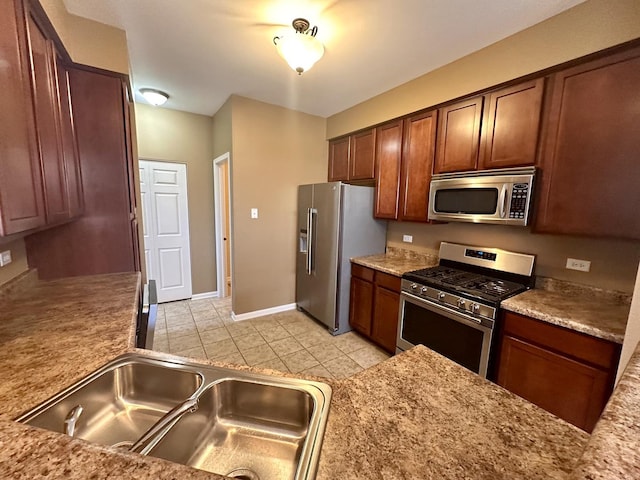 kitchen featuring appliances with stainless steel finishes, a sink, baseboards, and light tile patterned floors