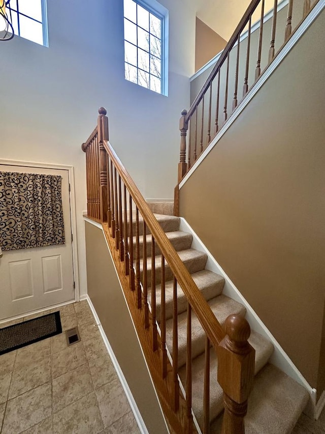 staircase featuring visible vents, a towering ceiling, and baseboards