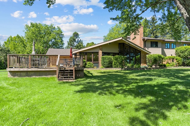 back of property with a chimney, a wooden deck, and a yard