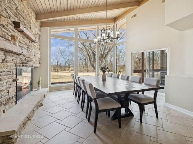 dining space with visible vents, baseboards, beamed ceiling, a stone fireplace, and wooden ceiling