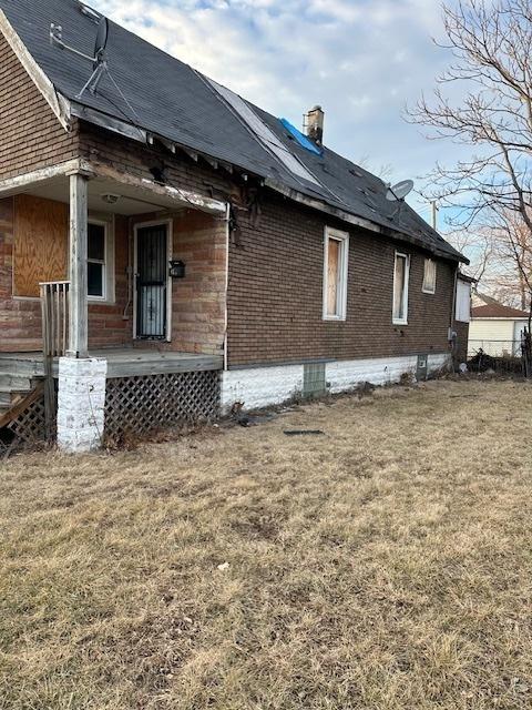 view of side of property with a porch, brick siding, a lawn, and a chimney