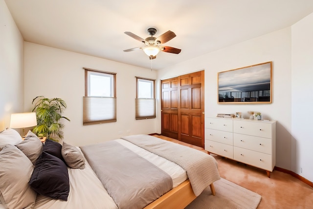 bedroom with a closet, baseboards, light colored carpet, and ceiling fan