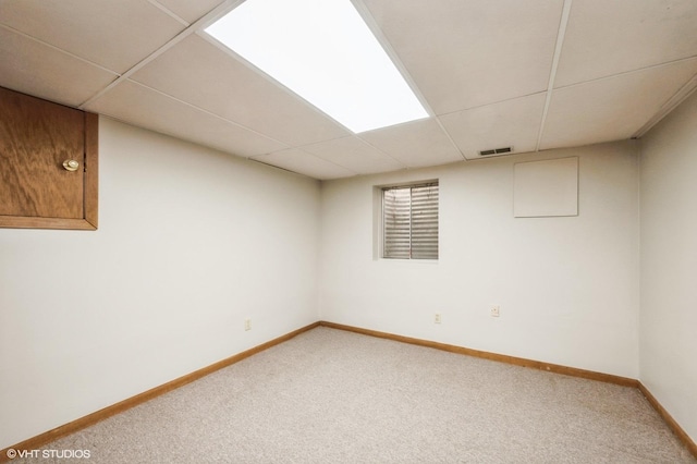 finished basement featuring visible vents, light colored carpet, baseboards, and a paneled ceiling