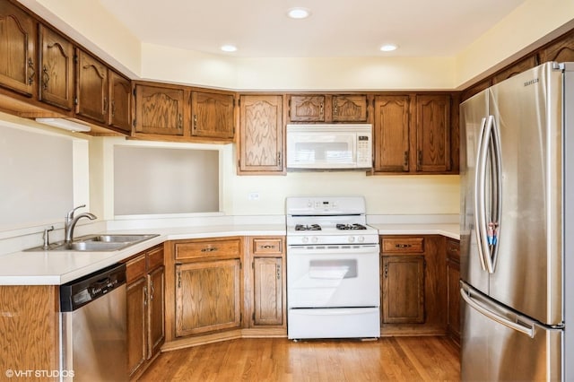 kitchen featuring brown cabinetry, light wood finished floors, a sink, light countertops, and appliances with stainless steel finishes