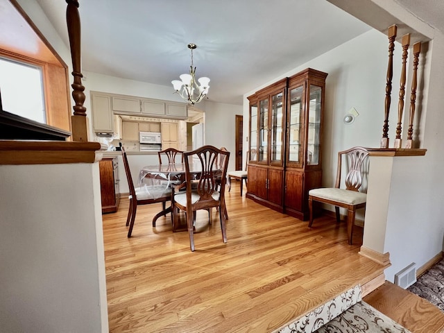 dining room featuring light wood-type flooring, baseboards, visible vents, and a chandelier