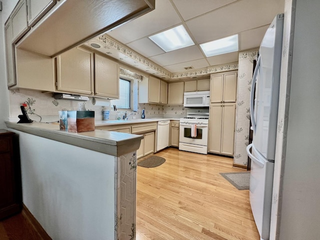 kitchen featuring white appliances, light wood-style flooring, a peninsula, light countertops, and a sink