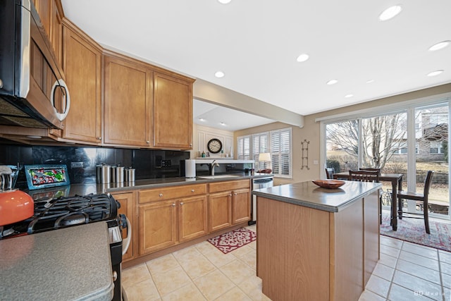 kitchen featuring brown cabinetry, decorative backsplash, dark countertops, stainless steel appliances, and a sink