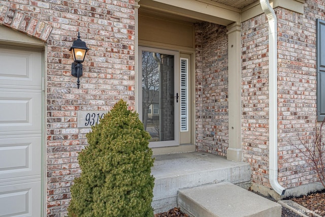 entrance to property featuring a garage, a porch, and brick siding