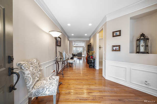 hallway featuring light wood-style floors, recessed lighting, a wainscoted wall, and crown molding