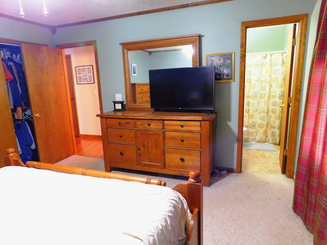 bedroom featuring connected bathroom, light carpet, a closet, a walk in closet, and crown molding