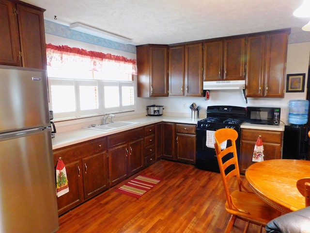 kitchen featuring dark wood-type flooring, under cabinet range hood, light countertops, black appliances, and a sink