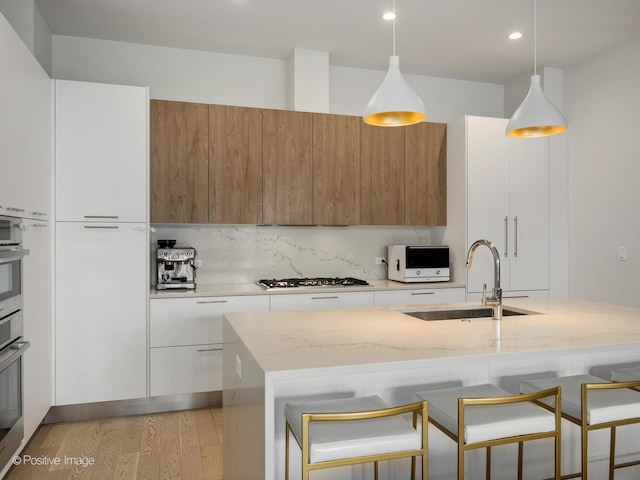 kitchen featuring light wood-type flooring, a kitchen bar, white appliances, modern cabinets, and a sink