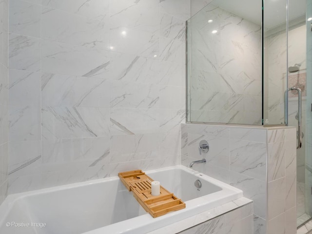 bathroom with a tile shower, a tub, and tile walls