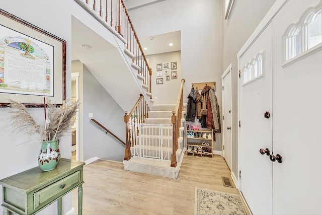 entryway with visible vents, a towering ceiling, stairs, baseboards, and light wood-type flooring