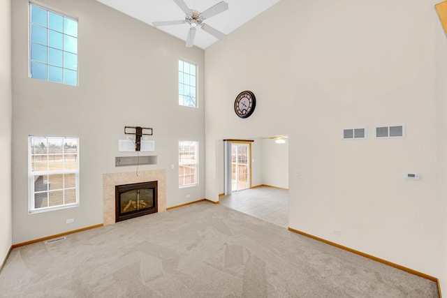 unfurnished living room featuring visible vents, a high ceiling, a ceiling fan, light carpet, and a tile fireplace