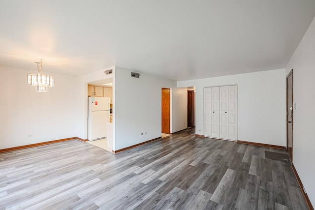 spare room with a chandelier, visible vents, light wood-style flooring, and baseboards