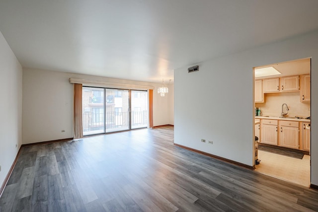 unfurnished living room featuring visible vents, an inviting chandelier, dark wood-type flooring, a sink, and baseboards