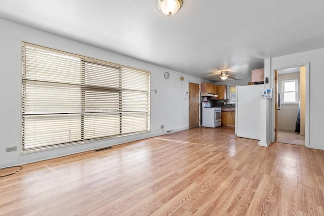 unfurnished living room with light wood-type flooring, baseboards, visible vents, and a ceiling fan