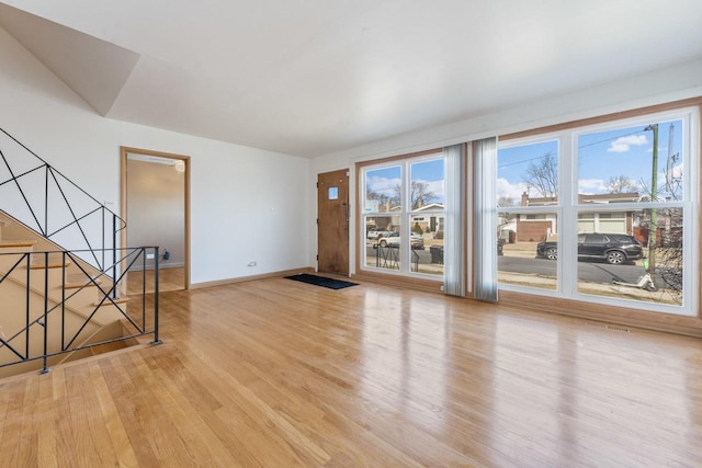 unfurnished living room featuring stairs, plenty of natural light, light wood-style flooring, and baseboards