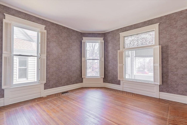 spare room with ornamental molding, visible vents, baseboards, and wood finished floors