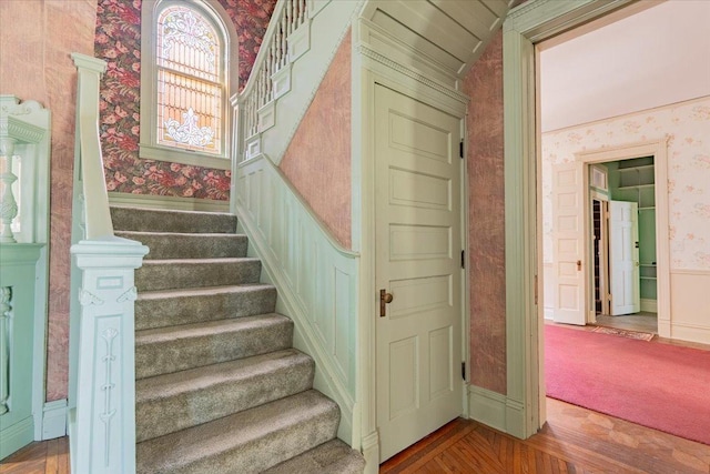 stairs with wood finished floors, a wainscoted wall, and wallpapered walls