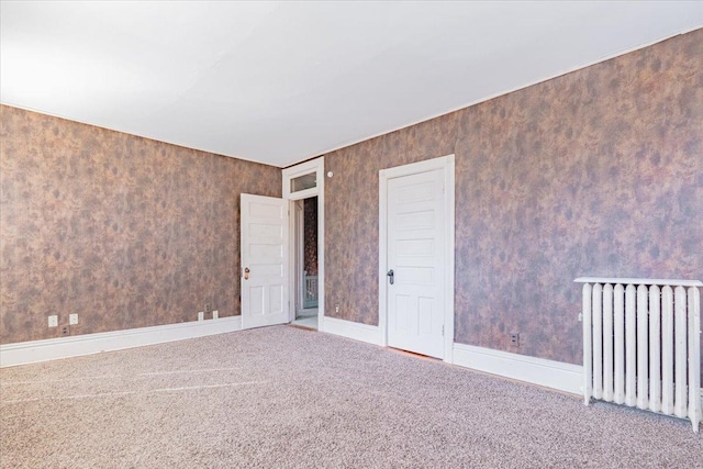 spare room with baseboards, carpet flooring, radiator heating unit, and wallpapered walls