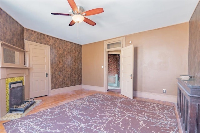 unfurnished living room featuring a ceiling fan, a fireplace with raised hearth, baseboards, and wood finished floors