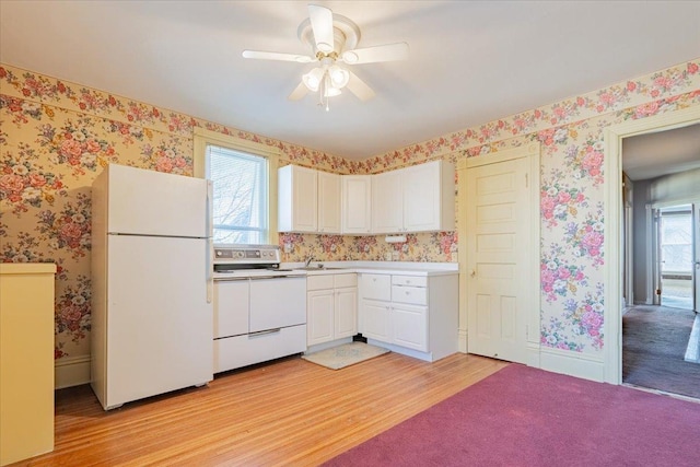 kitchen featuring white appliances, wallpapered walls, light wood-style floors, white cabinetry, and a sink