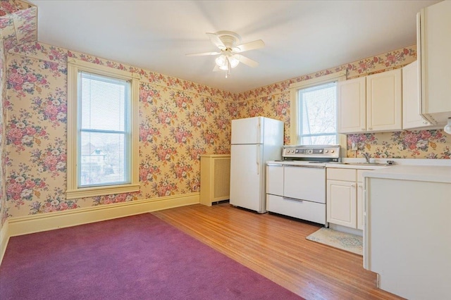 kitchen with white appliances, a sink, baseboards, light wood-type flooring, and wallpapered walls