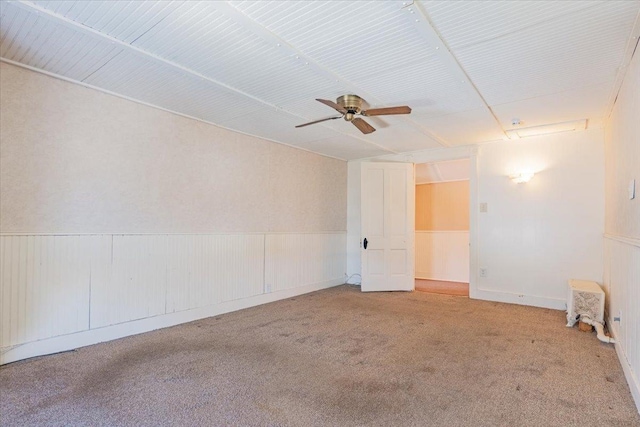 unfurnished room with carpet floors, a wainscoted wall, and ceiling fan