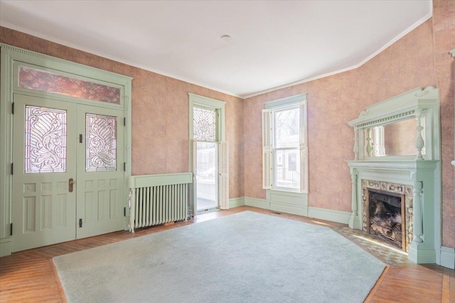 unfurnished living room with a fireplace, wood finished floors, french doors, ornamental molding, and radiator heating unit