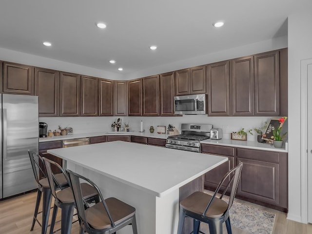 kitchen featuring a kitchen island, a breakfast bar, stainless steel appliances, light countertops, and light wood-style floors