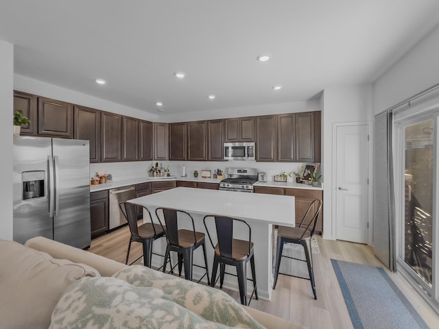 kitchen featuring a center island, stainless steel appliances, light countertops, dark brown cabinetry, and a kitchen bar