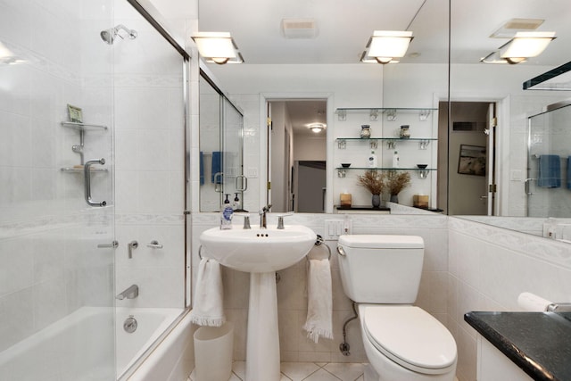 bathroom featuring combined bath / shower with glass door, tile patterned floors, toilet, and tile walls