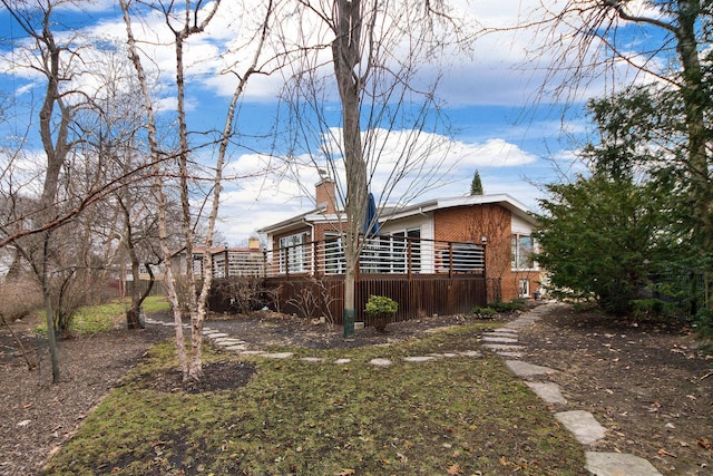 view of home's exterior featuring a wooden deck, a chimney, and brick siding