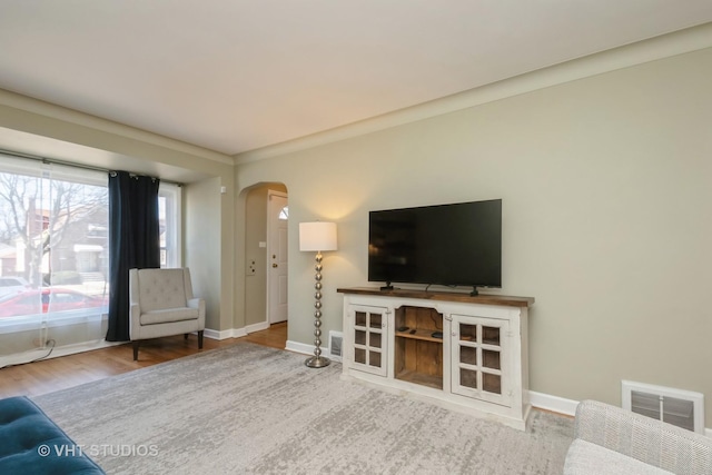 unfurnished living room with wood finished floors, arched walkways, visible vents, and baseboards