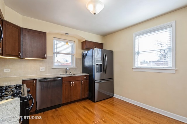 kitchen with light wood finished floors, backsplash, baseboards, appliances with stainless steel finishes, and a sink