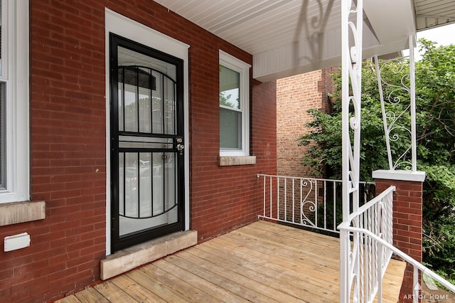 view of exterior entry featuring covered porch and brick siding