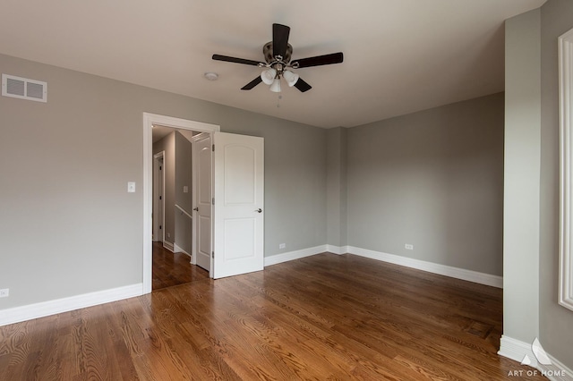 empty room with dark wood-style floors, visible vents, ceiling fan, and baseboards