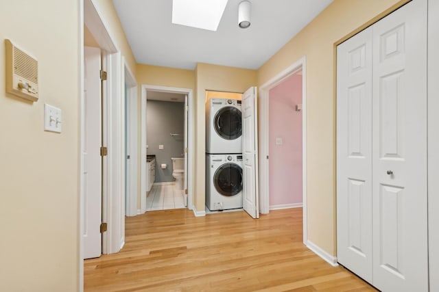 laundry room featuring a skylight, laundry area, baseboards, stacked washer and clothes dryer, and light wood-style floors