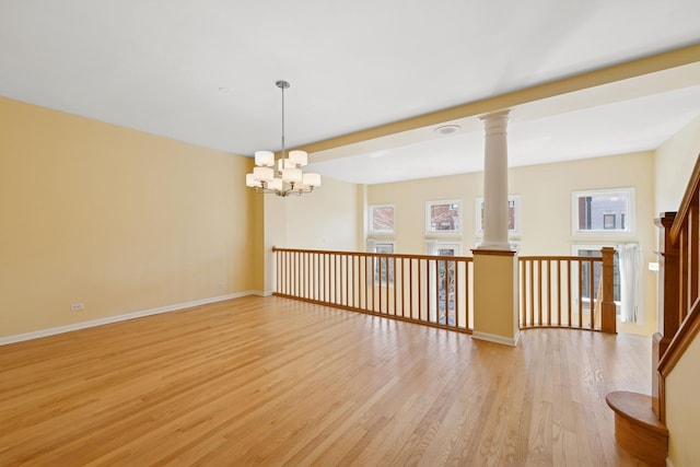 empty room featuring ornate columns, light wood finished floors, an inviting chandelier, and baseboards