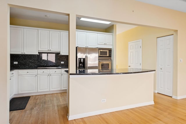 kitchen featuring appliances with stainless steel finishes, white cabinetry, light wood finished floors, and decorative backsplash