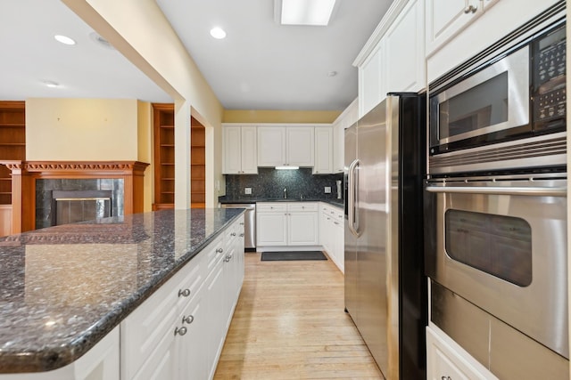 kitchen featuring stainless steel appliances, tasteful backsplash, light wood-style floors, a high end fireplace, and white cabinetry