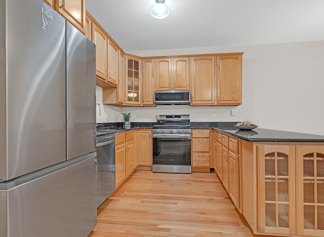 kitchen featuring appliances with stainless steel finishes, glass insert cabinets, a peninsula, light brown cabinetry, and light wood-type flooring