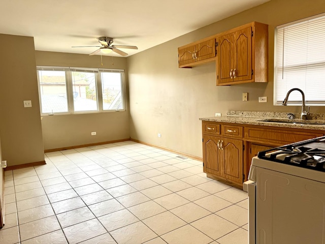 kitchen with a sink, a ceiling fan, baseboards, brown cabinetry, and gas range gas stove