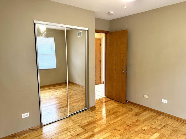 unfurnished bedroom featuring a closet, visible vents, baseboards, and light wood finished floors