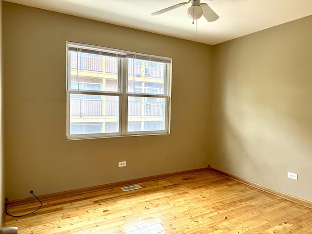 spare room featuring light wood finished floors, baseboards, visible vents, and a ceiling fan