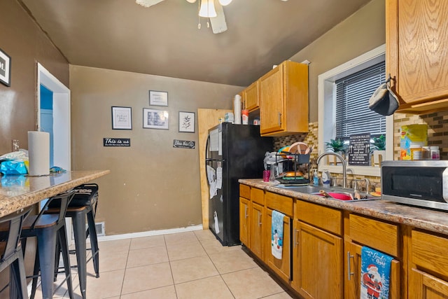 kitchen featuring tasteful backsplash, freestanding refrigerator, stainless steel microwave, and a sink