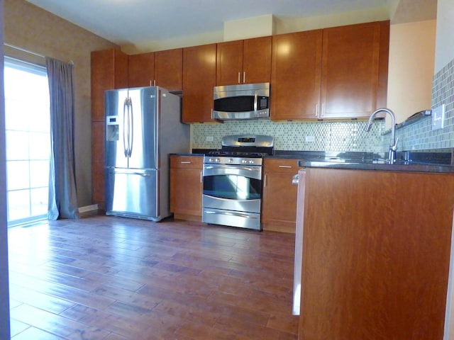 kitchen with dark wood-style flooring, dark countertops, backsplash, appliances with stainless steel finishes, and brown cabinetry