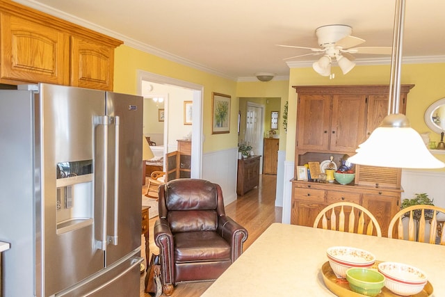 dining space with light wood-style flooring, ceiling fan, crown molding, and wainscoting